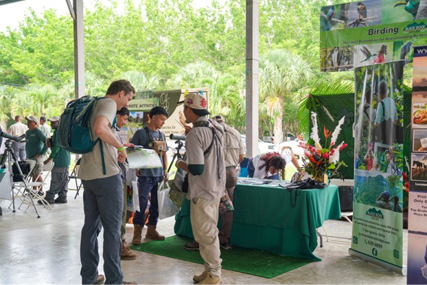 Visitors interacting with guides and viewing materials at a birding exhibit during an outdoor event in Belize.