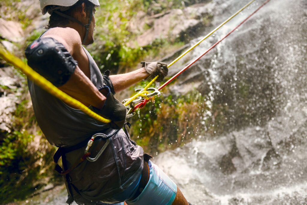 A close-up shot of an adventurer wearing safety gear and gloves while participating in Belize waterfall rappelling.